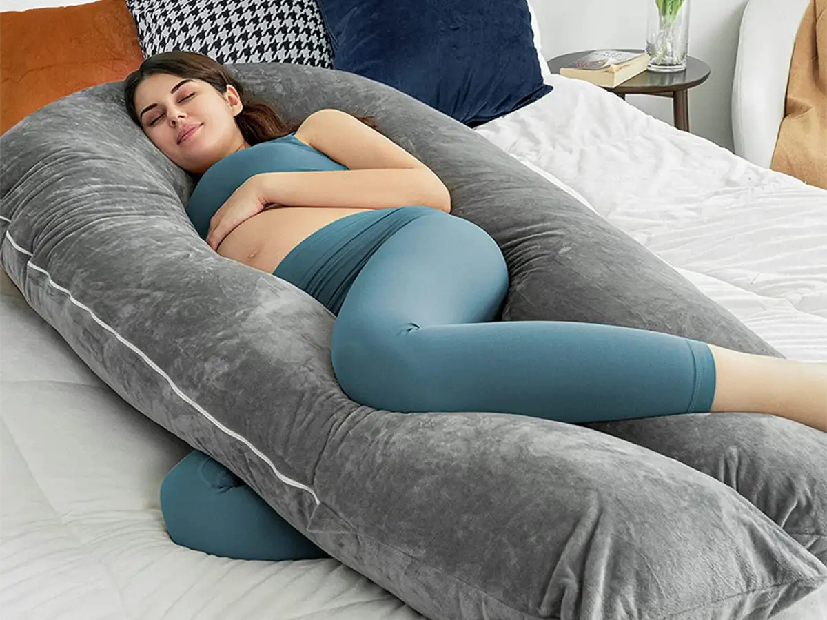 A pregnant woman comfortably rests on her side in bed, enveloped by the Body Massager Velvet U Shaped Pregnancy Pillow.